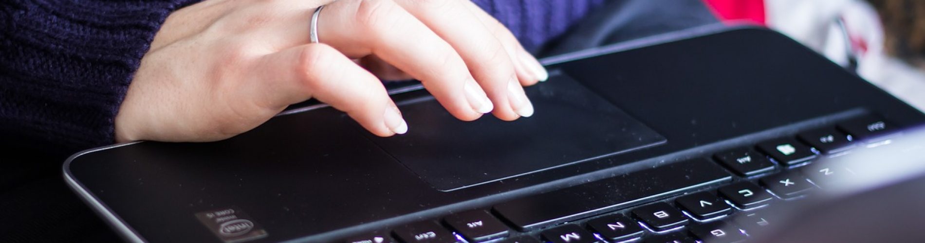 a woman with with blue jumper and rings on her hand typing on a black laptop